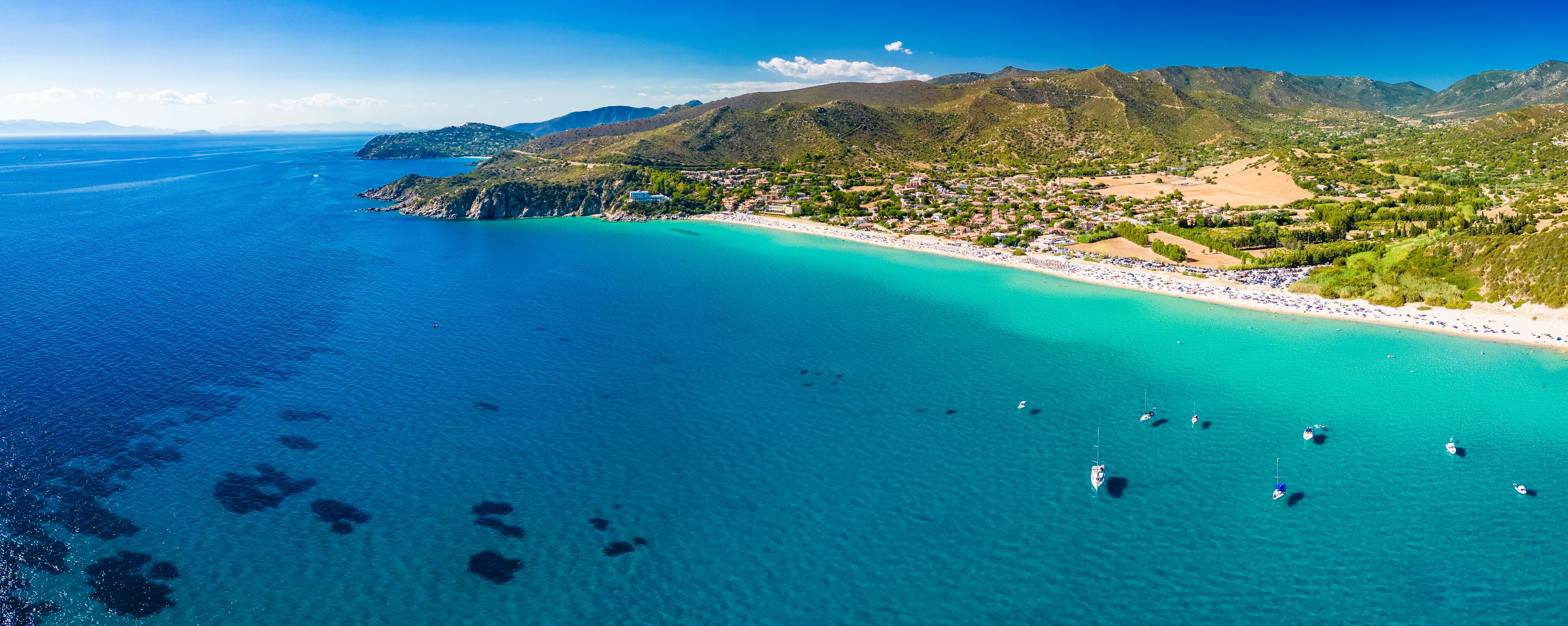 Een kustplaatsje met een strand, boten en bergen.