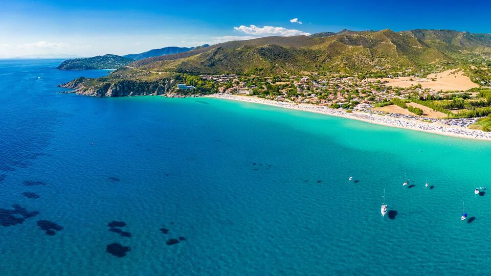 Een kustplaatsje met een strand, boten en bergen.