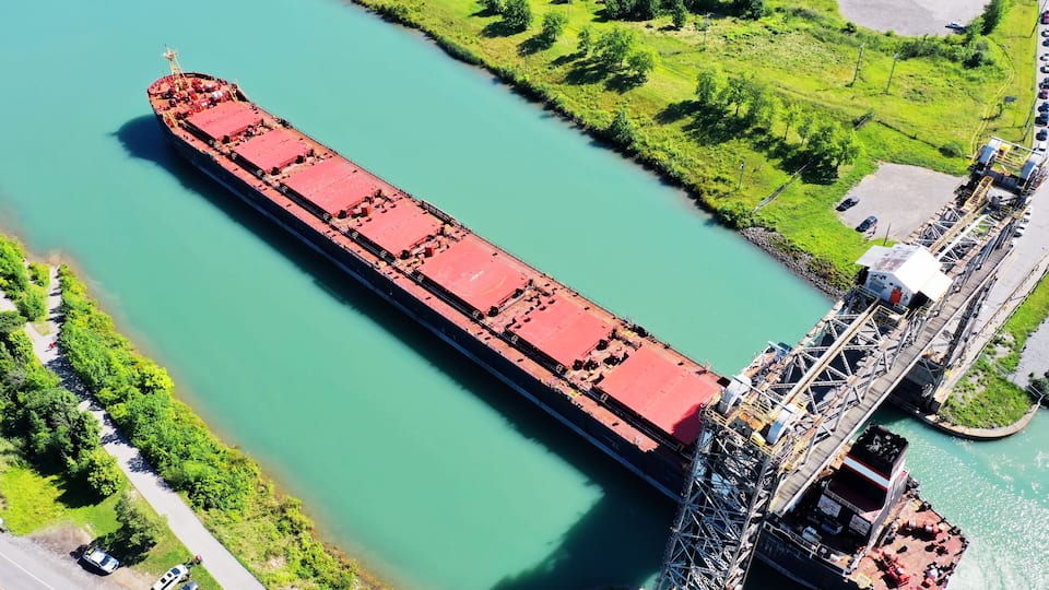A large cargo ship on a river, a bridge, and a parking area with cars.