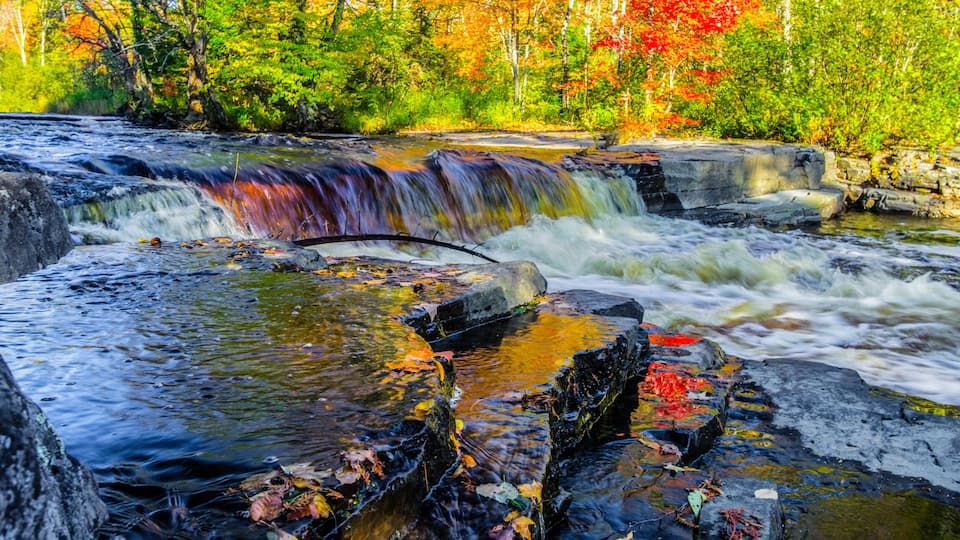 A waterfall cascading over rocks in a forested area with autumn foliage.