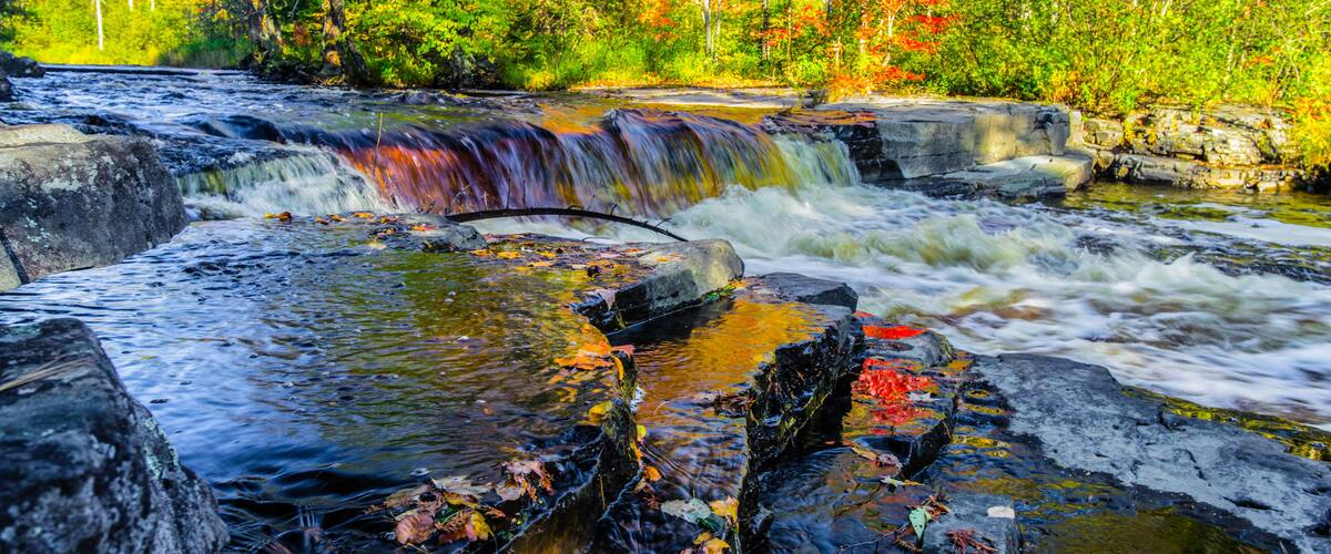 A waterfall cascading over rocks in a forested area with autumn foliage.