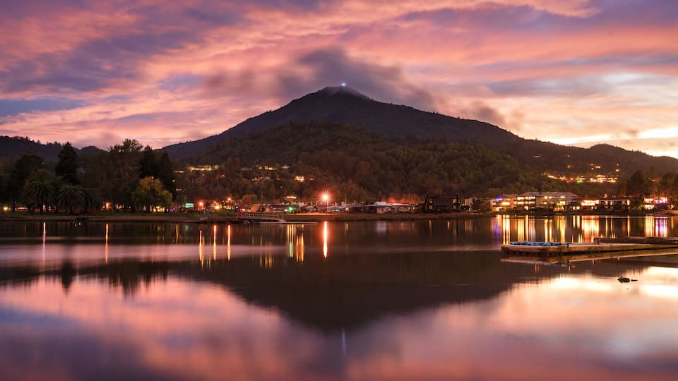 A mountain at dusk with a lake reflecting lights and a dock.