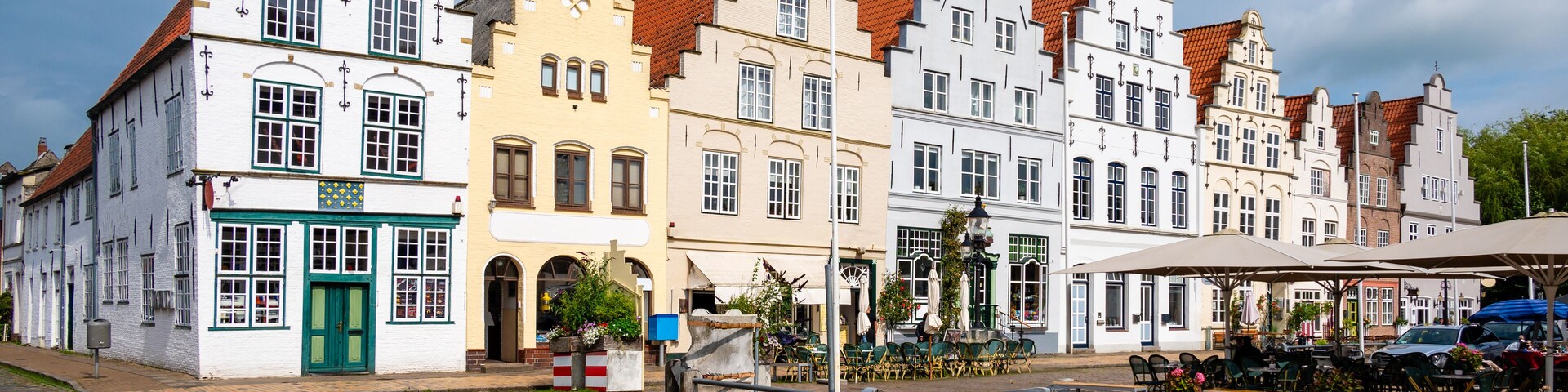 Rua de paraleipípedos ladeada por edifícios históricos com estilos arquitetônicos distintos e uma área de estar coberta ao ar livre.