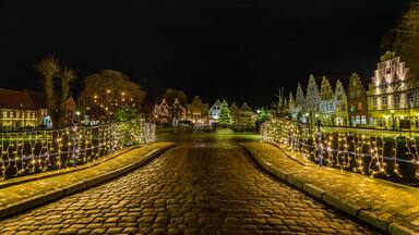 A cobblestone street at night with festive lights and a Christmas tree.
