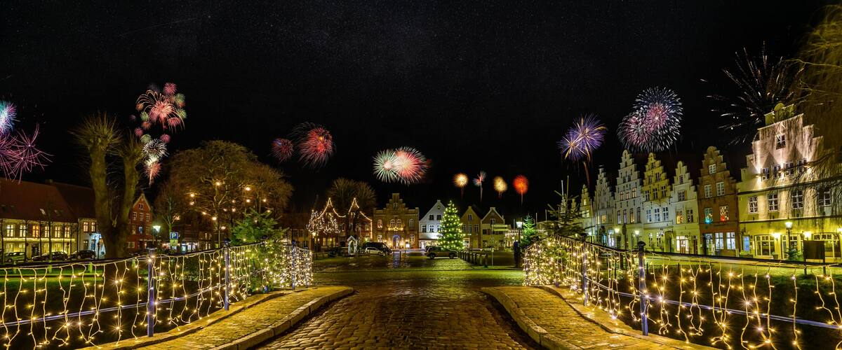 A cobblestone street with festive lights and a Christmas tree.