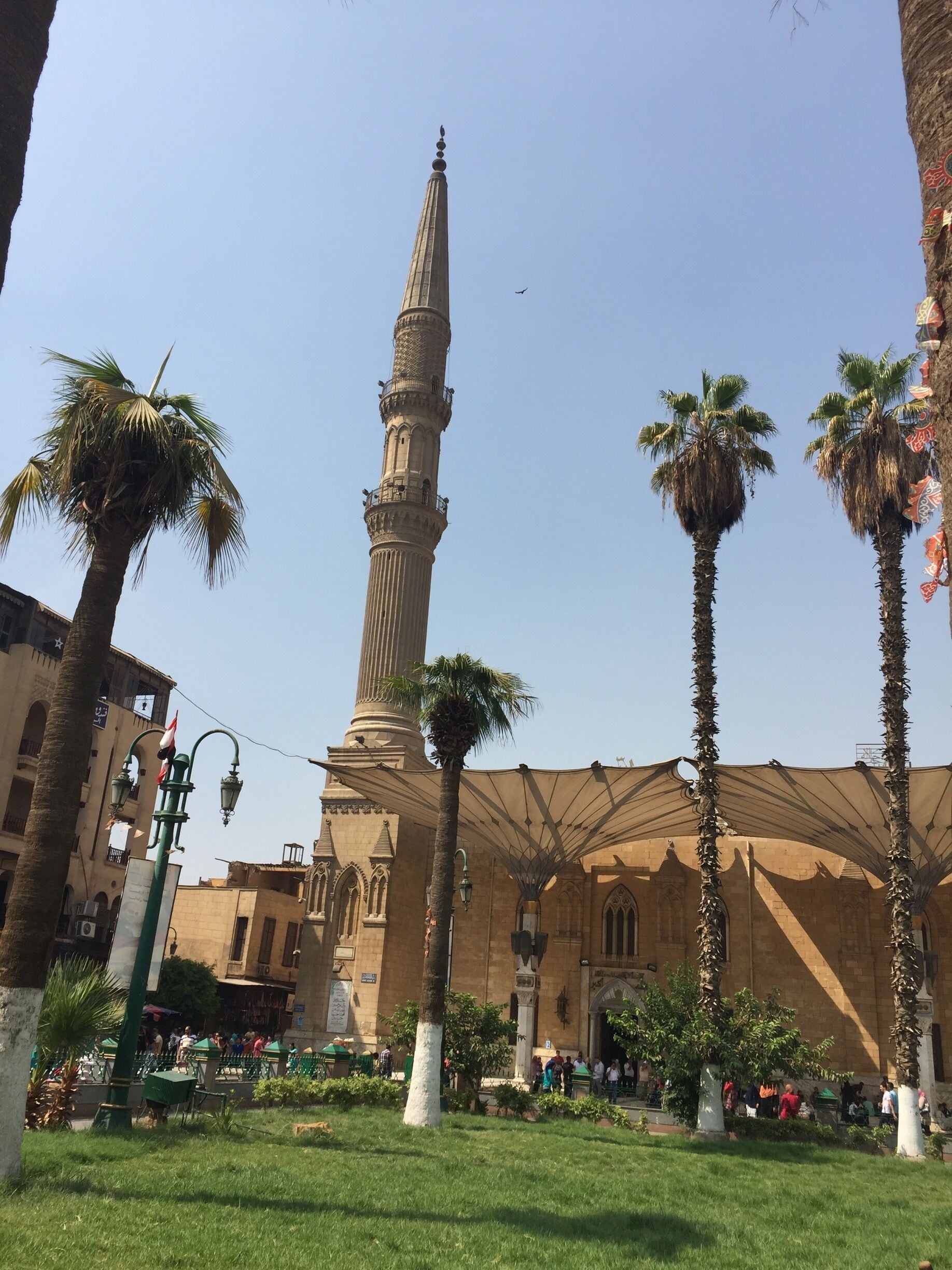 Una mezquita con un minarete alto, palmeras y un cielo azul despejado.