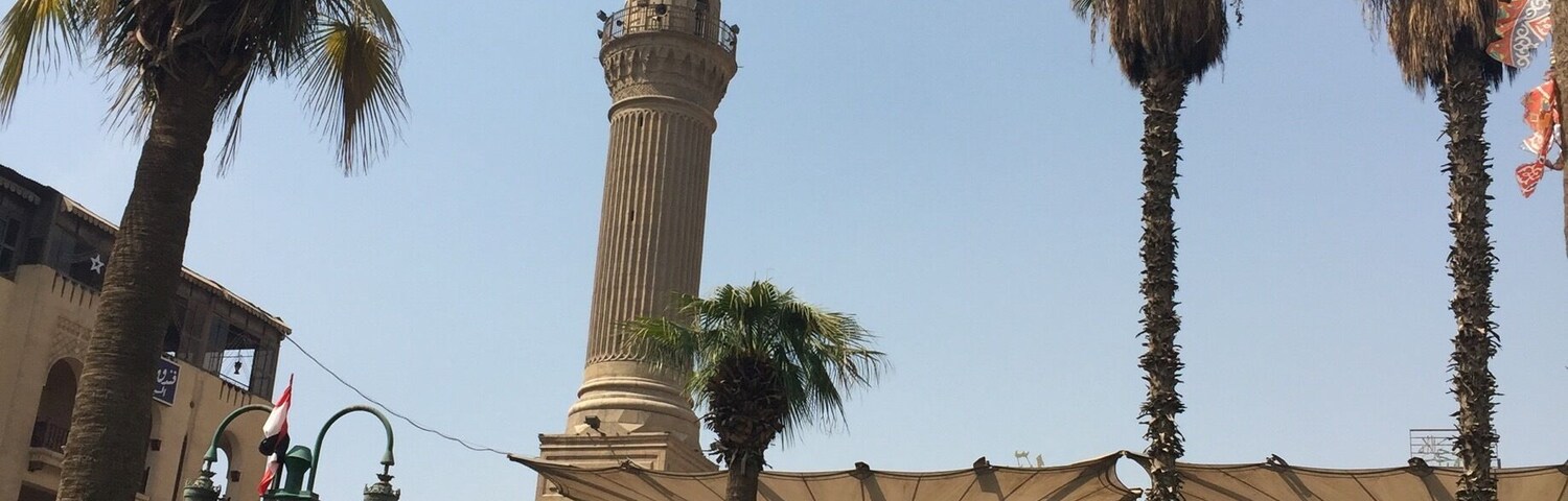 Una mezquita con un minarete alto, palmeras y un cielo azul despejado.