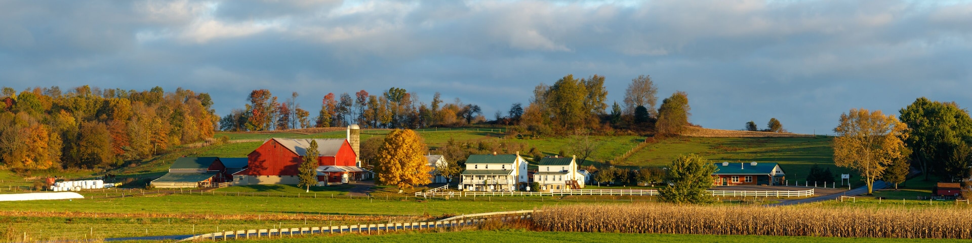 A rural landscape with a barn, farmhouse, and rolling hills.