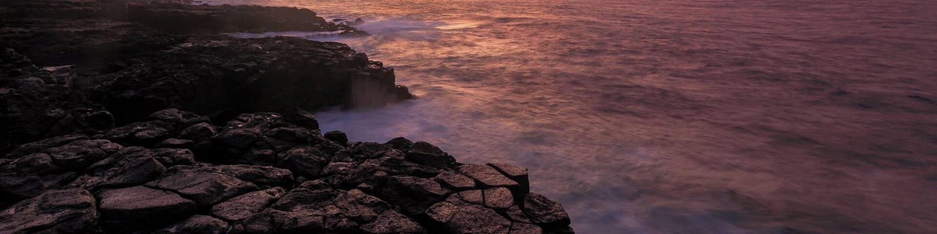 A rocky shoreline with a sunset over the ocean.
