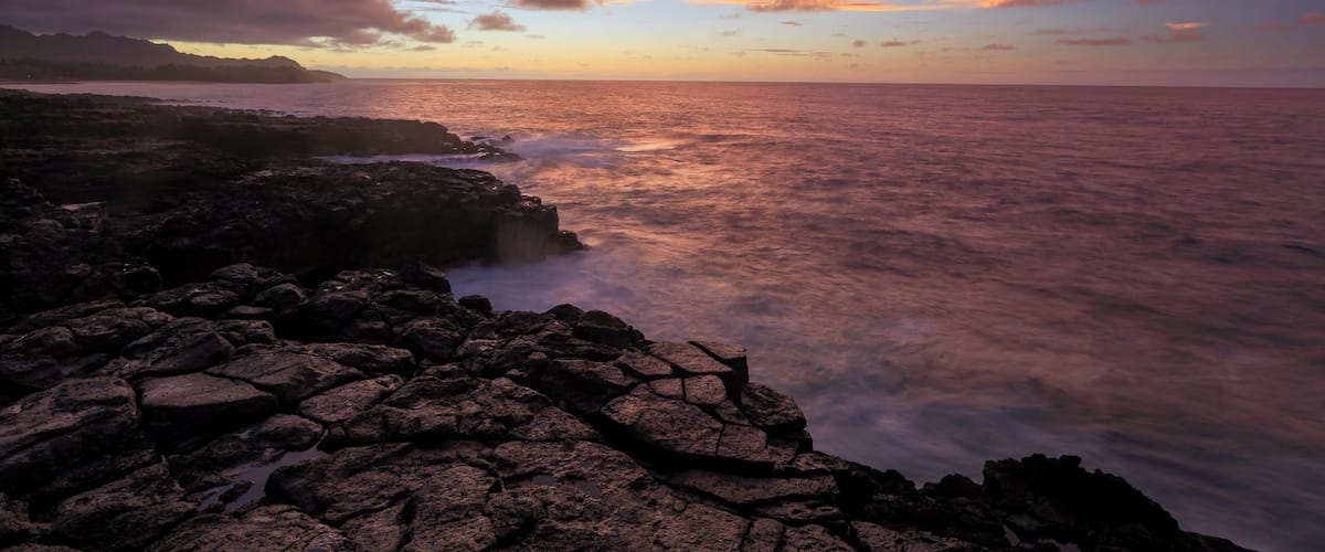 A rocky shoreline with a sunset over the ocean.
