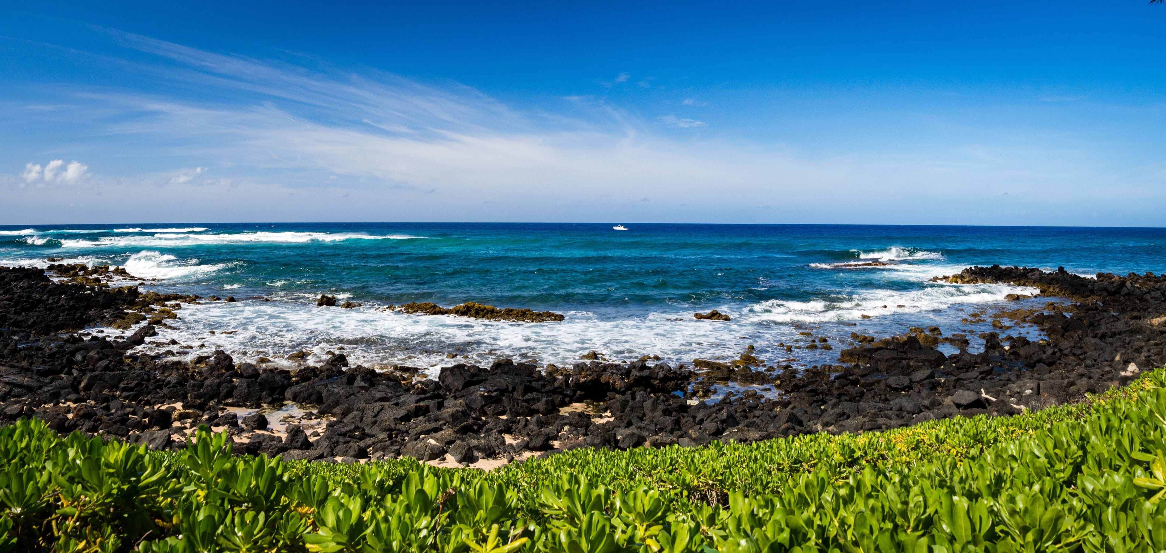 A rocky coastline with waves crashing against the shore and a clear blue sky.