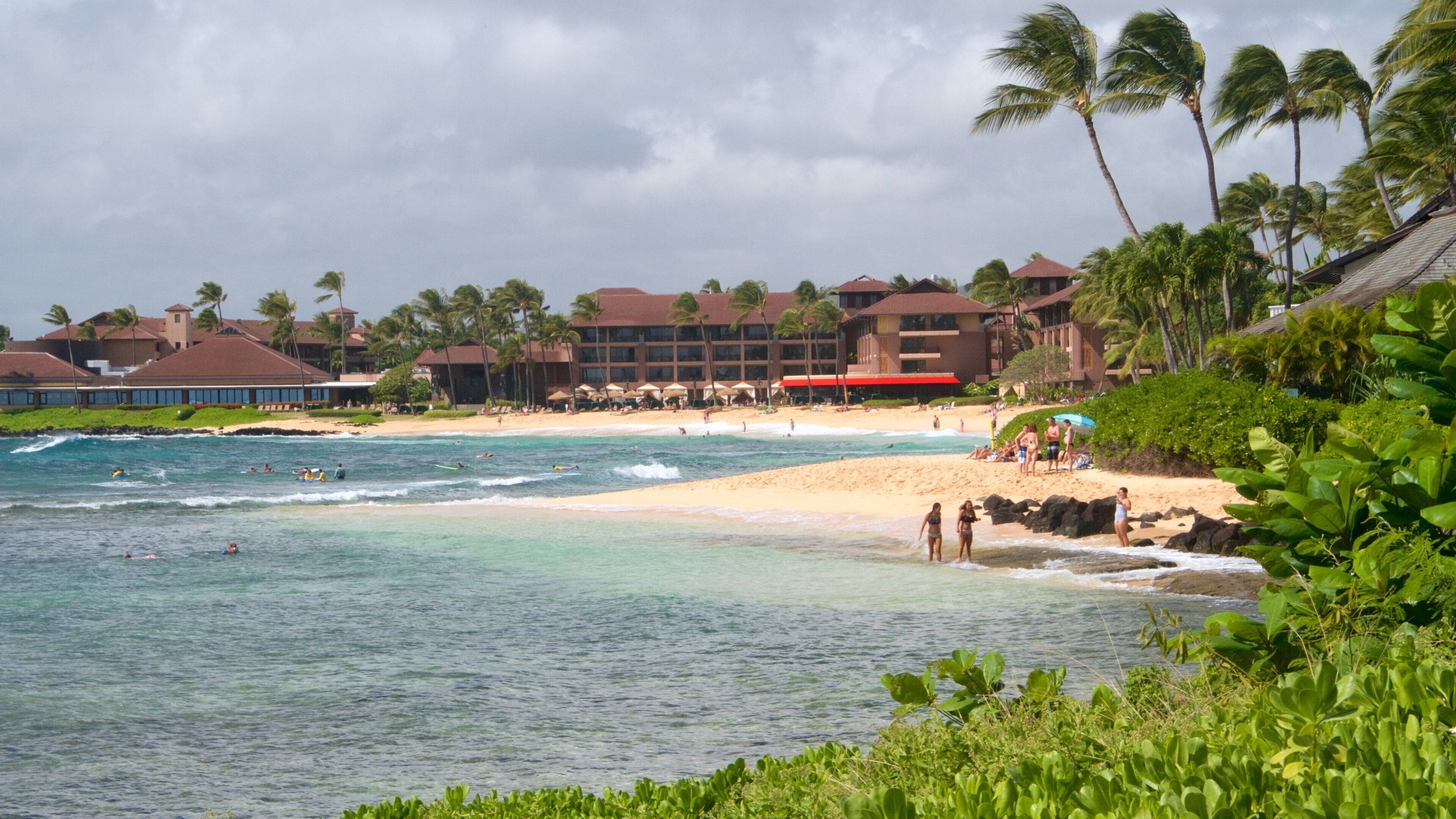 A beach with clear turquoise water, palm trees, and a resort in the background.