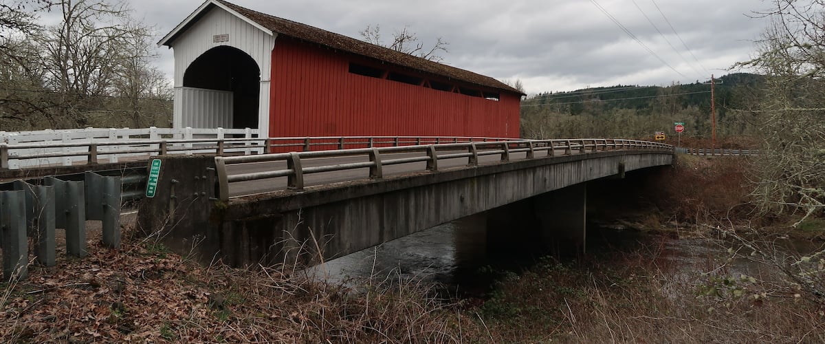A covered bridge with a red roof and white walls crossing a river.