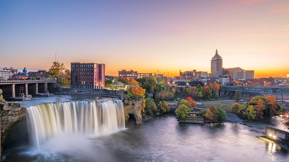 A waterfall, a bridge, and a city skyline at sunset.