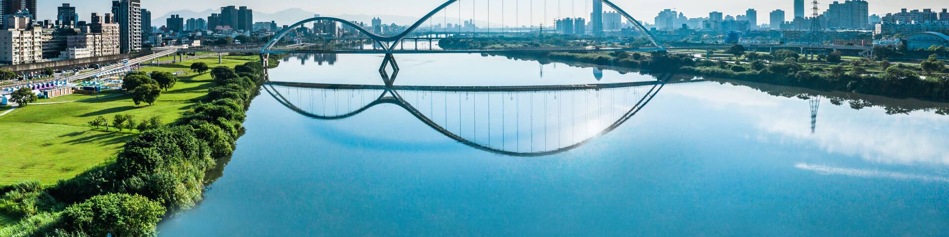 Un paisaje urbano con un puente grande sobre un río tranquilo que refleja el horizonte.