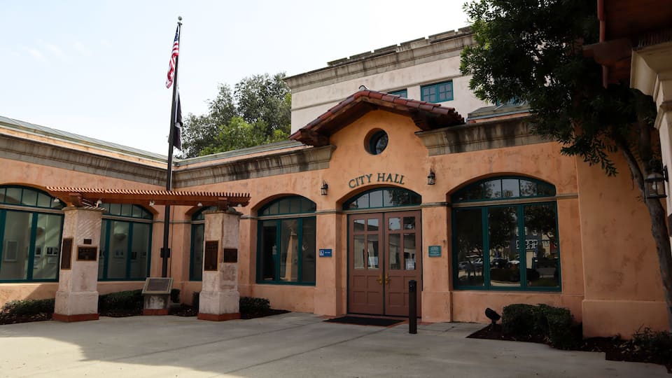 A building with a sign reading 'City Hall,' featuring a traditional architectural style with a tiled roof and arched windows.