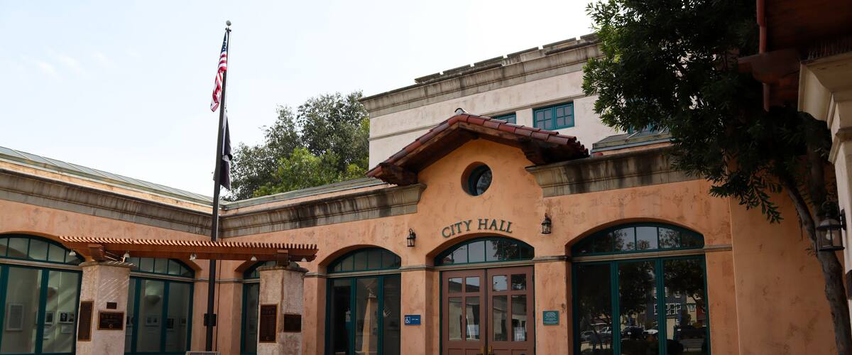 A building with a sign reading 'City Hall,' featuring a traditional architectural style with a tiled roof and arched windows.