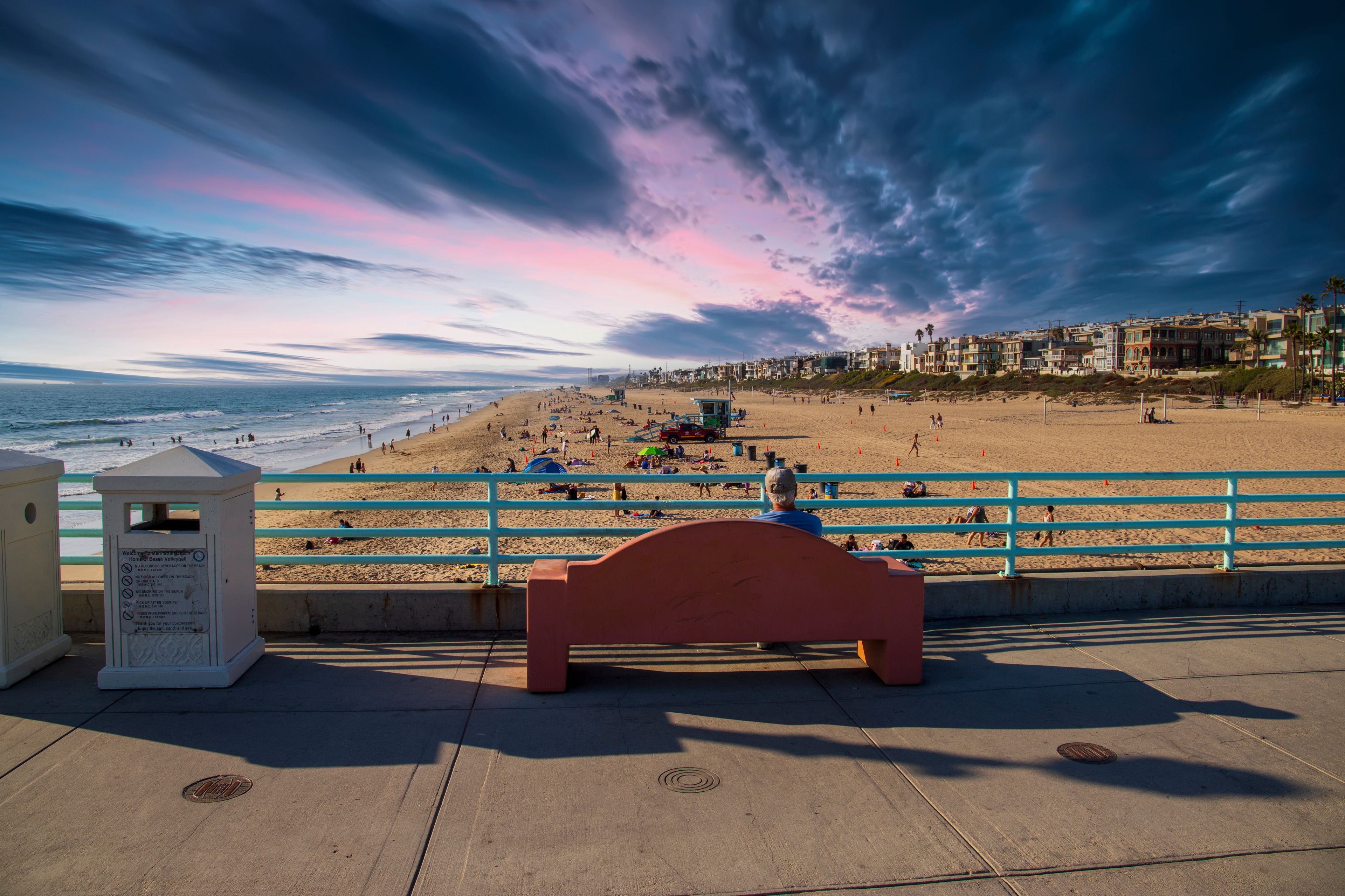 A beach with a bench, a lifeguard tower, and a row of colorful houses in the background.