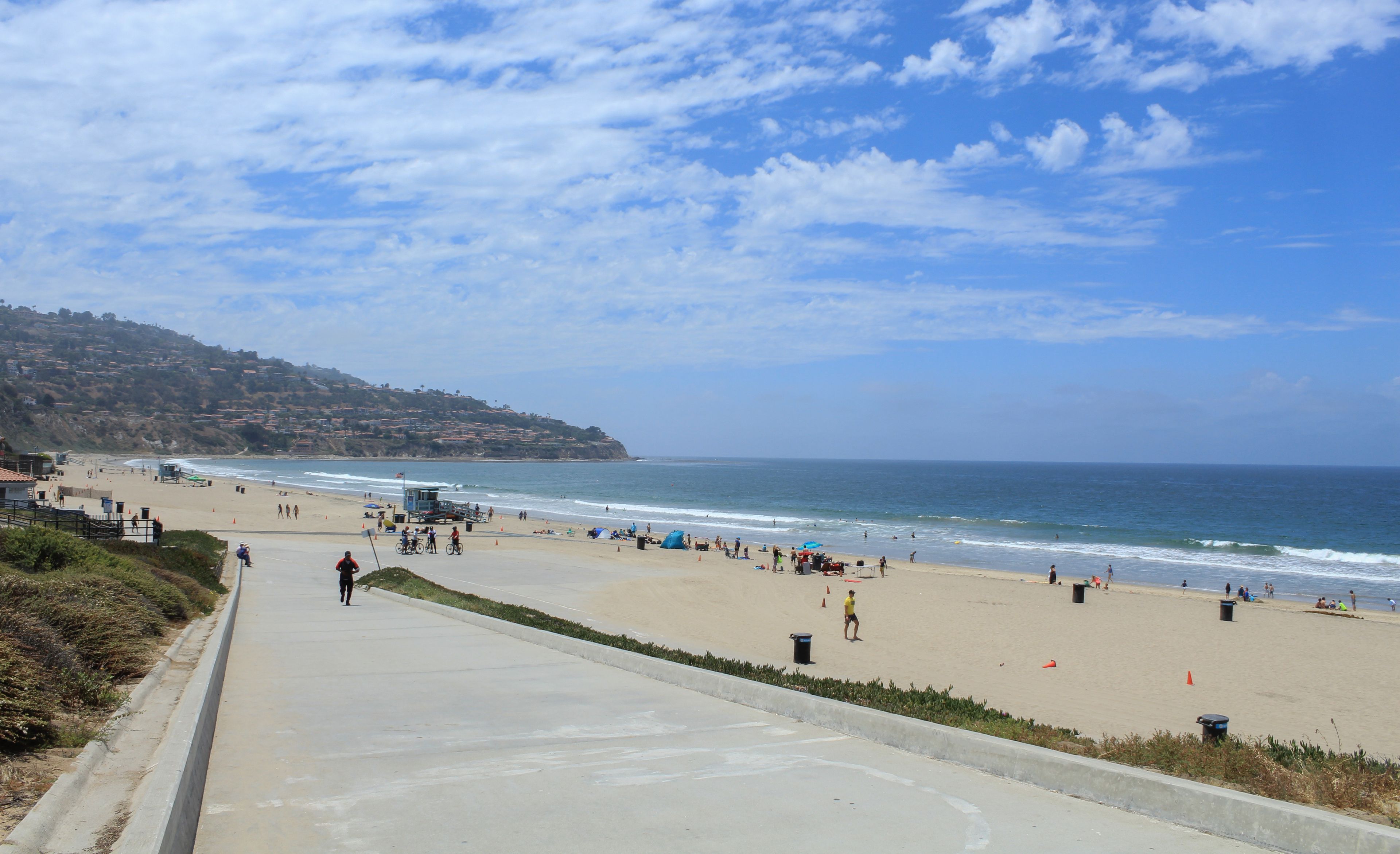 A coastal beach with a clear sky, a sandy shore, and a hilly landscape in the background.