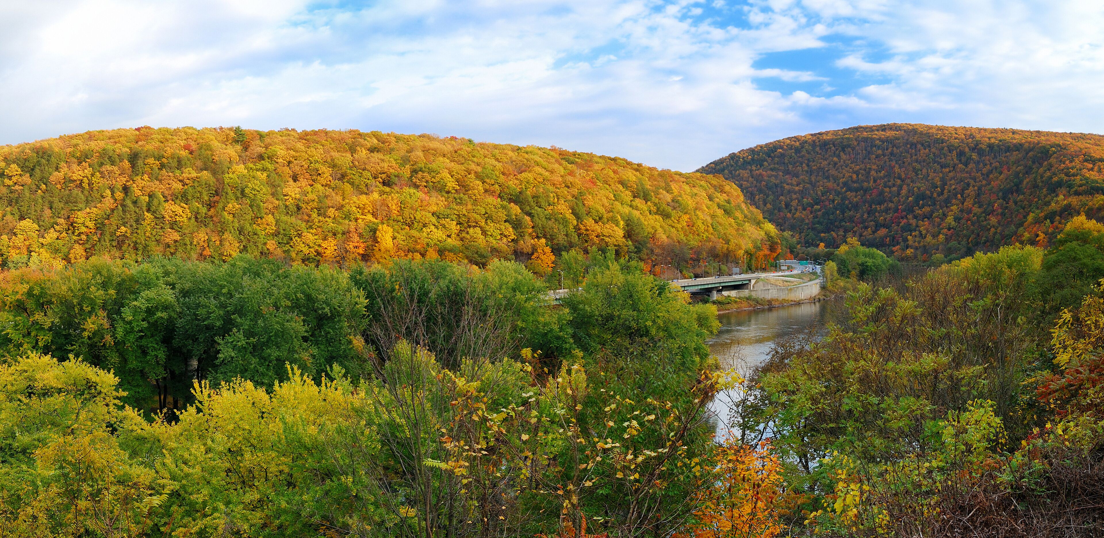 A river with a bridge, surrounded by autumn-colored trees and hills.