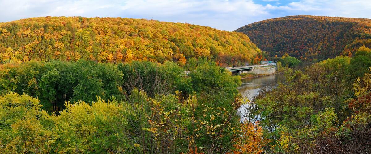 A river with a bridge, surrounded by autumn-colored trees and hills.