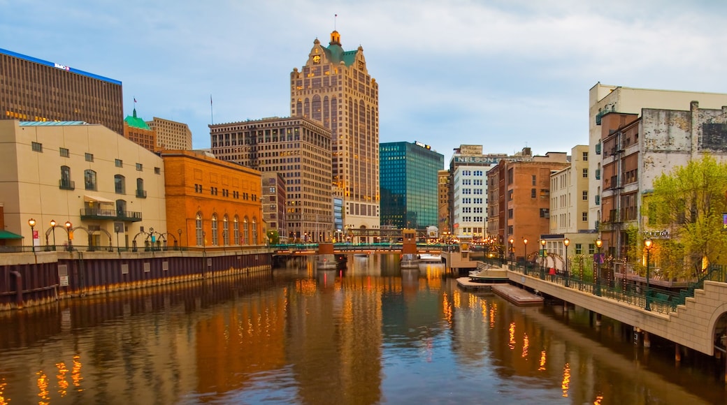 A river with buildings reflecting on the water, a bridge, and a tall building with a green roof.