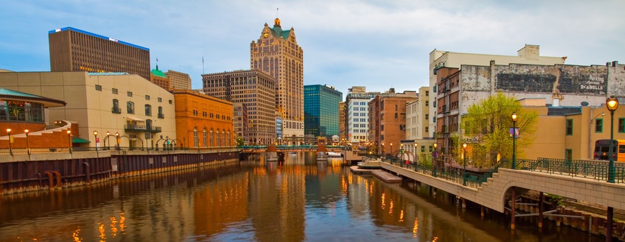 A river with buildings reflecting on the water, a bridge, and a tall building with a green roof.