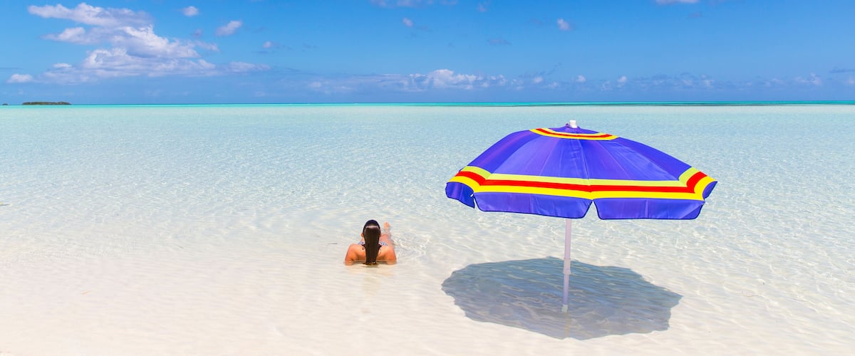 A clear blue sky, a sandy beach, and a person relaxing under a colorful umbrella.