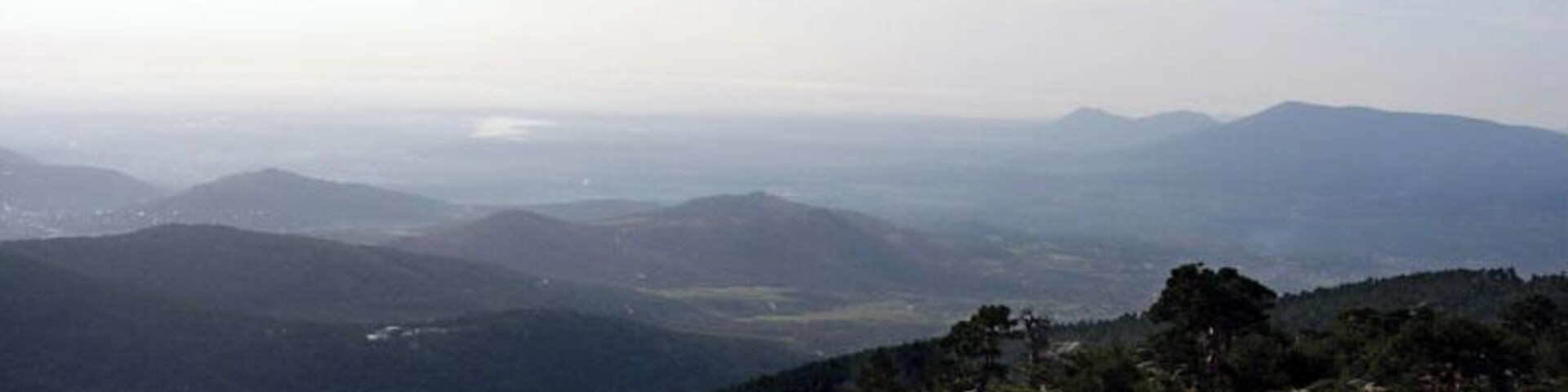 Un paisaje montañoso con colinas onduladas y árboles dispersos.