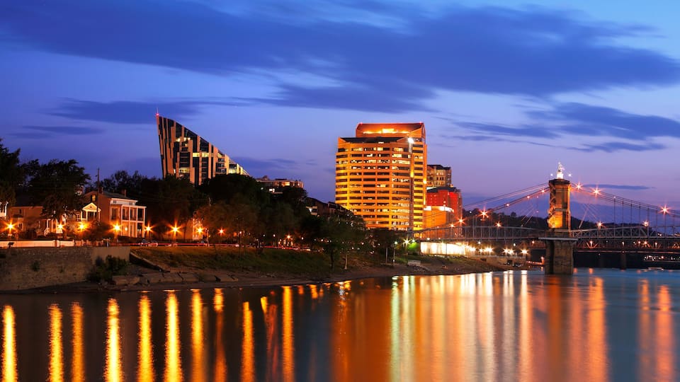 A river with a bridge, modern buildings, and a lit-up skyline at dusk.