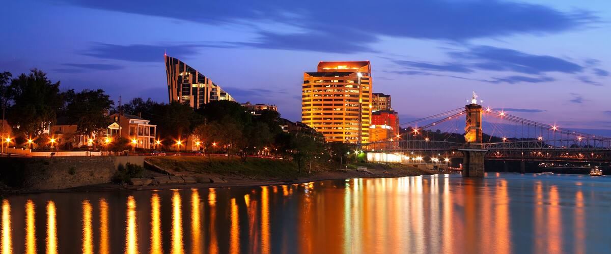 A river with a bridge, modern buildings, and a lit-up skyline at dusk.