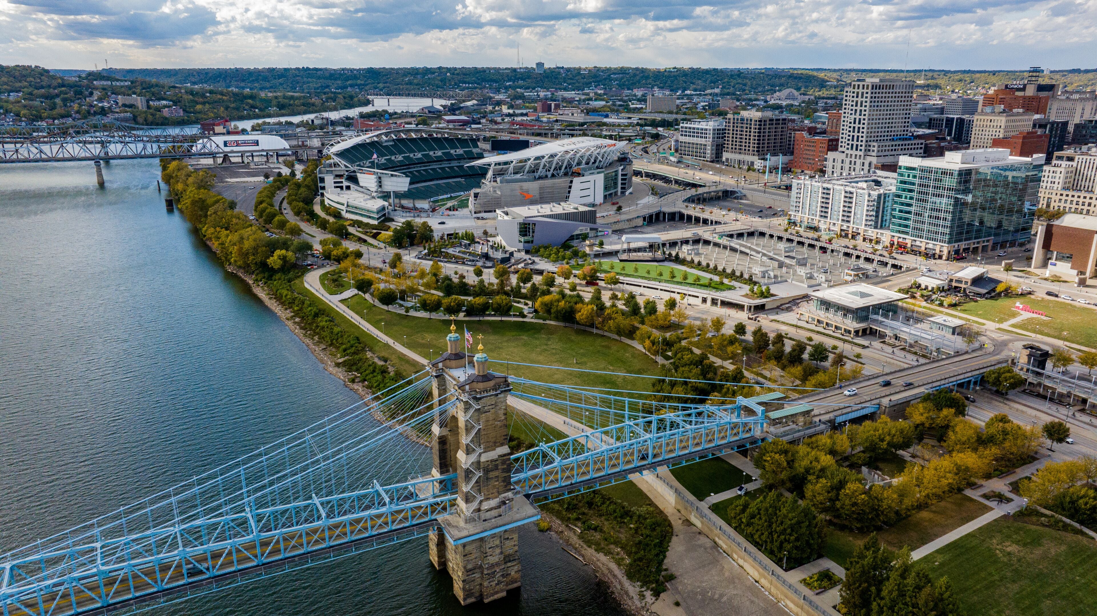 Aerial view of the John A. Roebling Suspension Bridge over the Ohio River, with Paycor Stadium and the cityscape contrasting against the autumnal trees, Covington, Kentucky, United States.