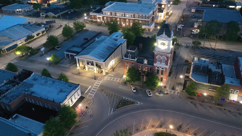 An aerial view of a town square with a prominent clock tower, a large building with a dome, and a roundabout.