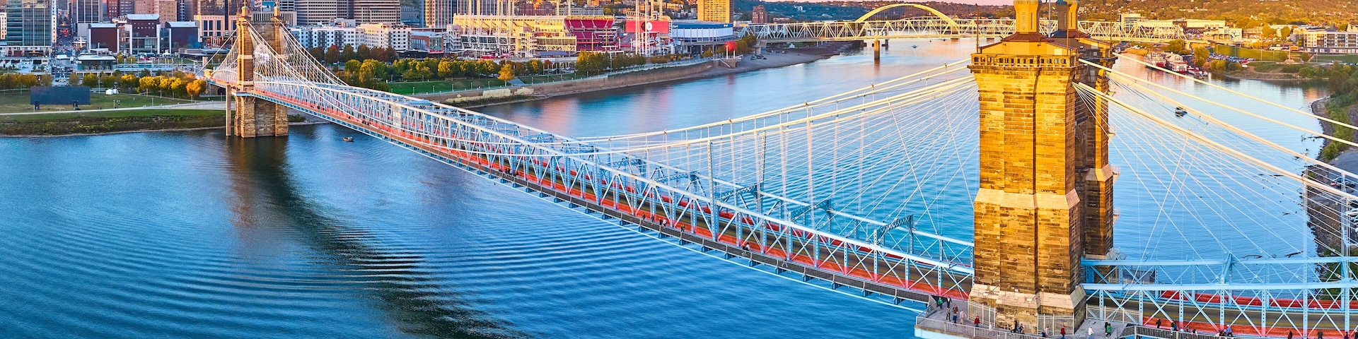 Un puente colgante sobre un río con el perfil urbano de una ciudad al fondo.