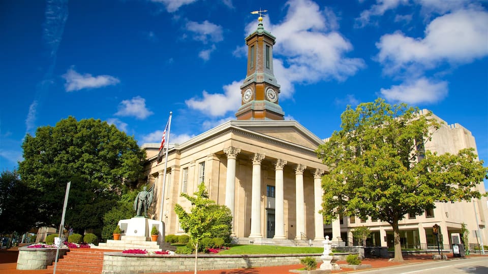 A historic building with a clock tower, columns, and a statue in front.