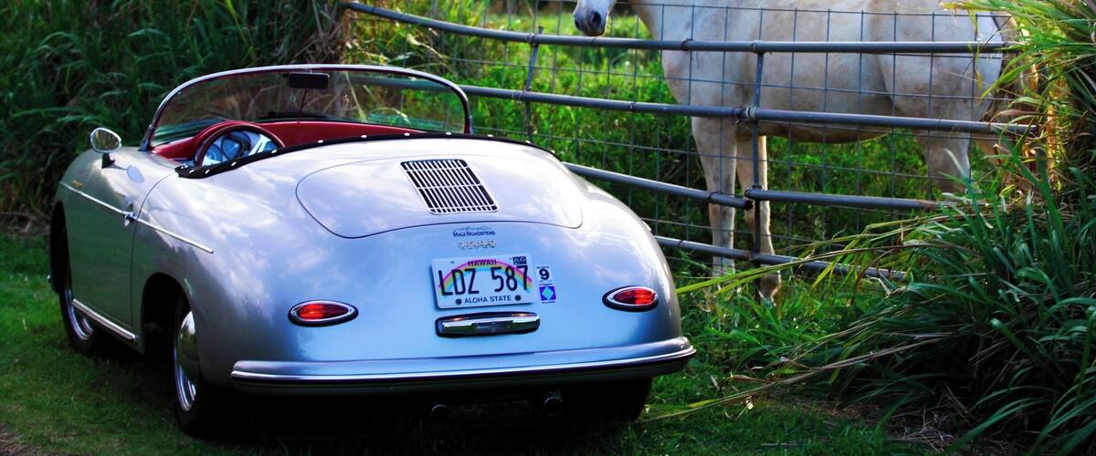 A vintage convertible car parked near a fence with a horse in the background.