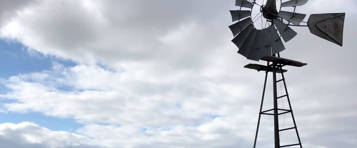 A windmill in a barren landscape with snow patches and a cloudy sky.
