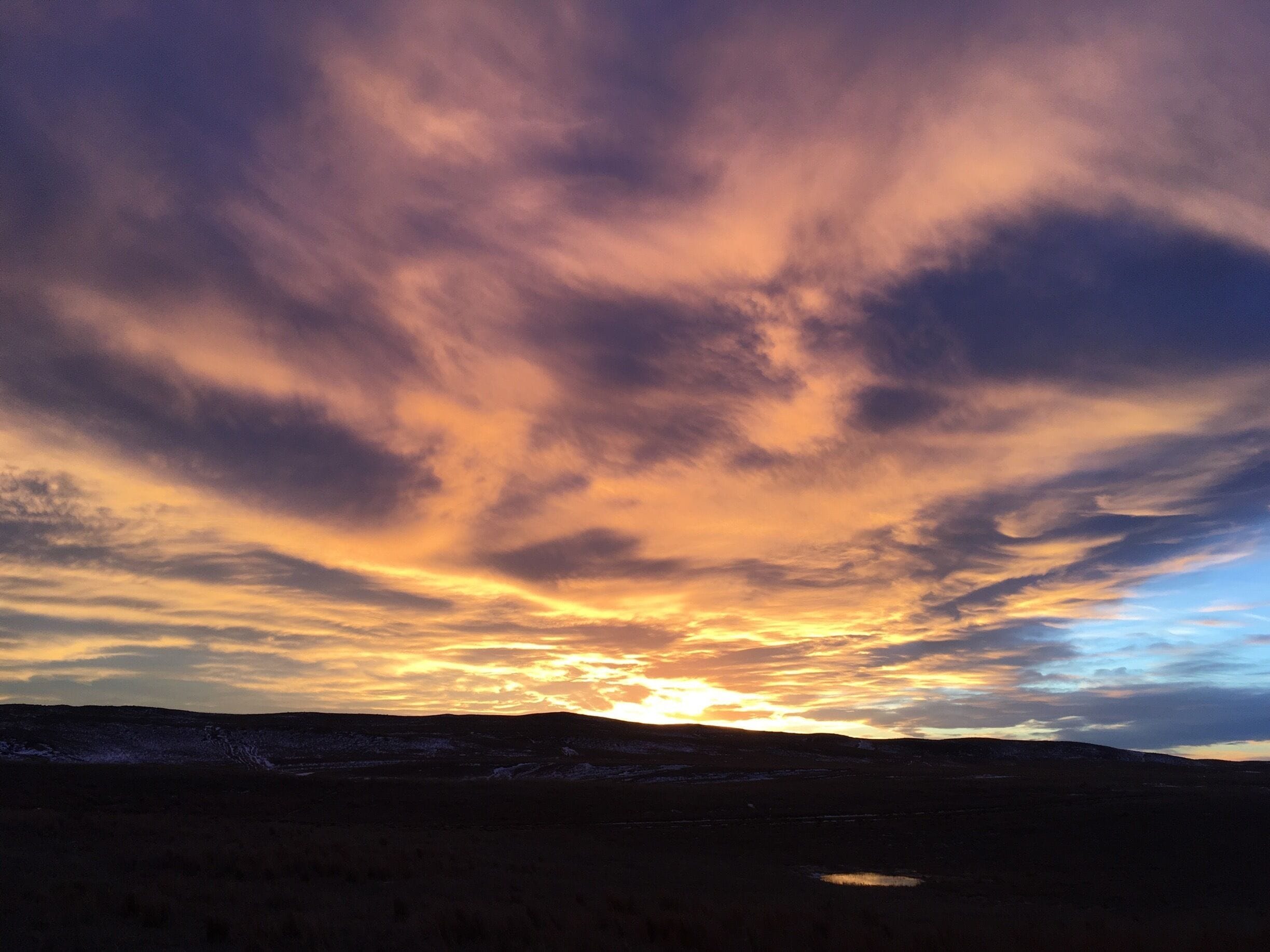 A sunset over a mountainous landscape with a small lake.