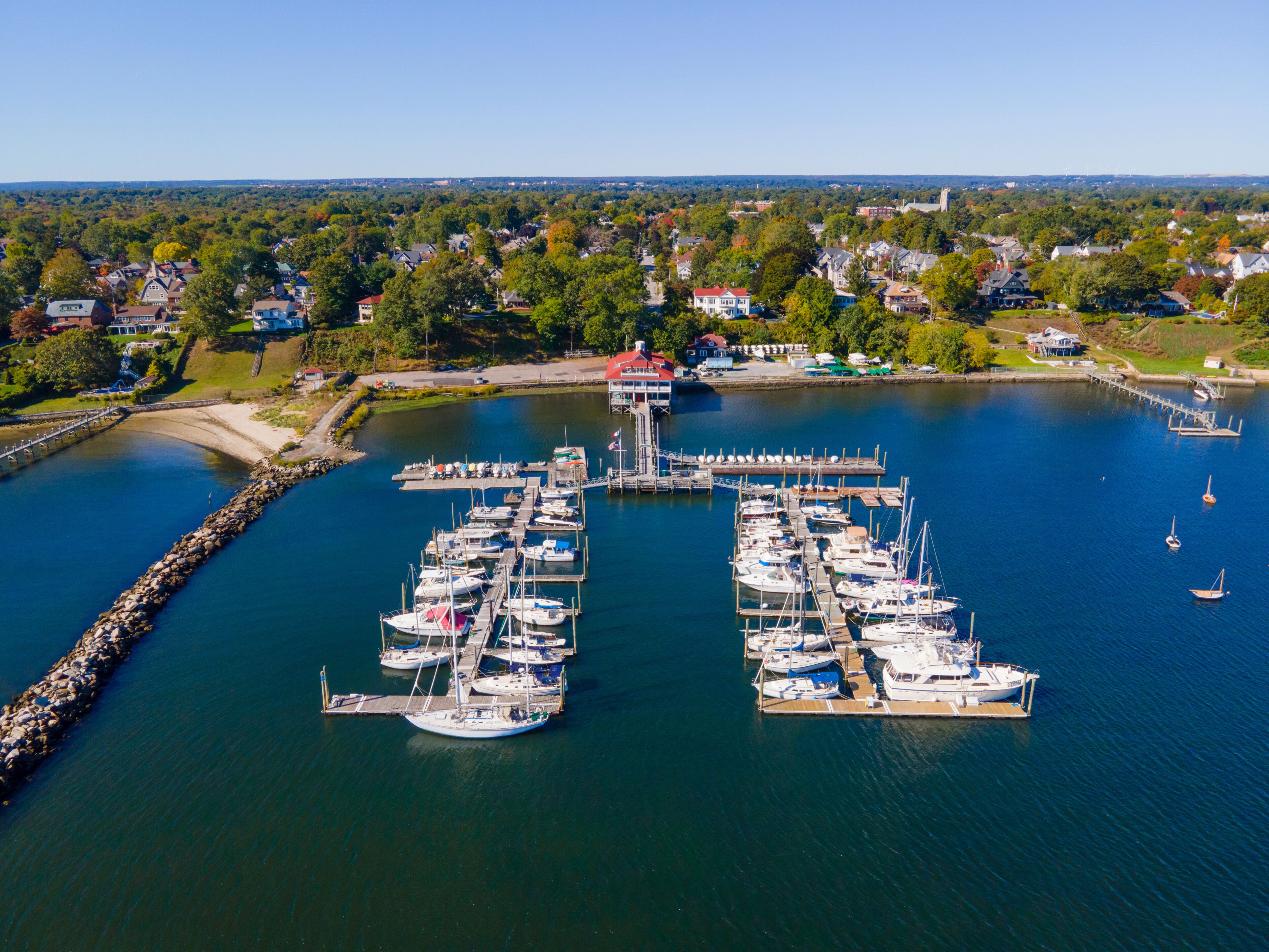 A marina with multiple boats docked, surrounded by a residential area and a clear sky.