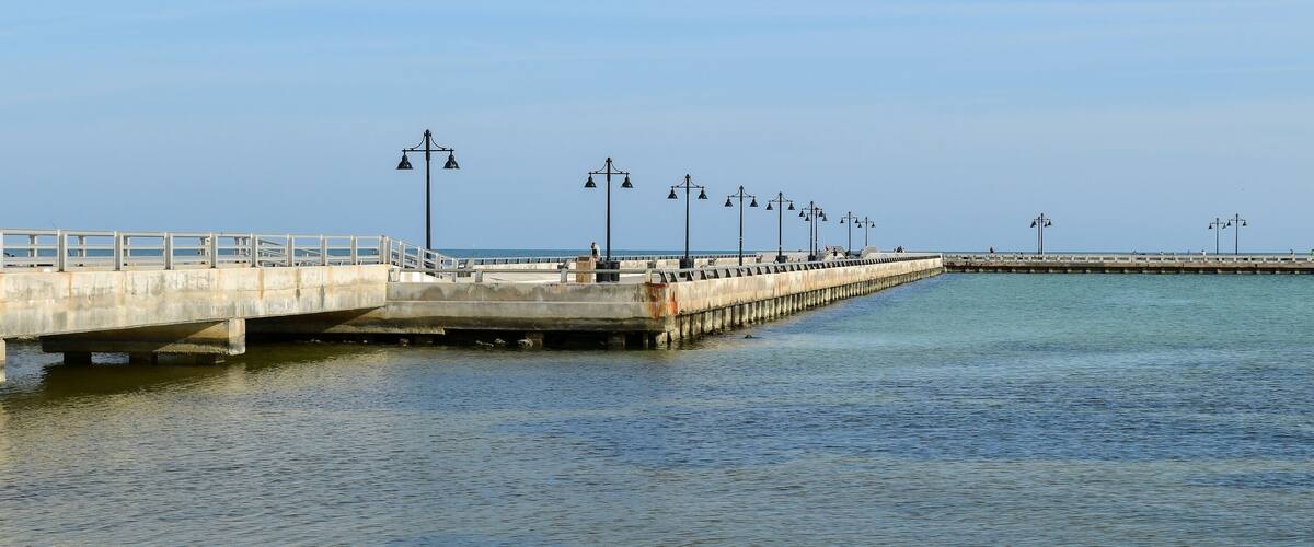 A concrete pier extending into calm waters with street lamps and a railing.