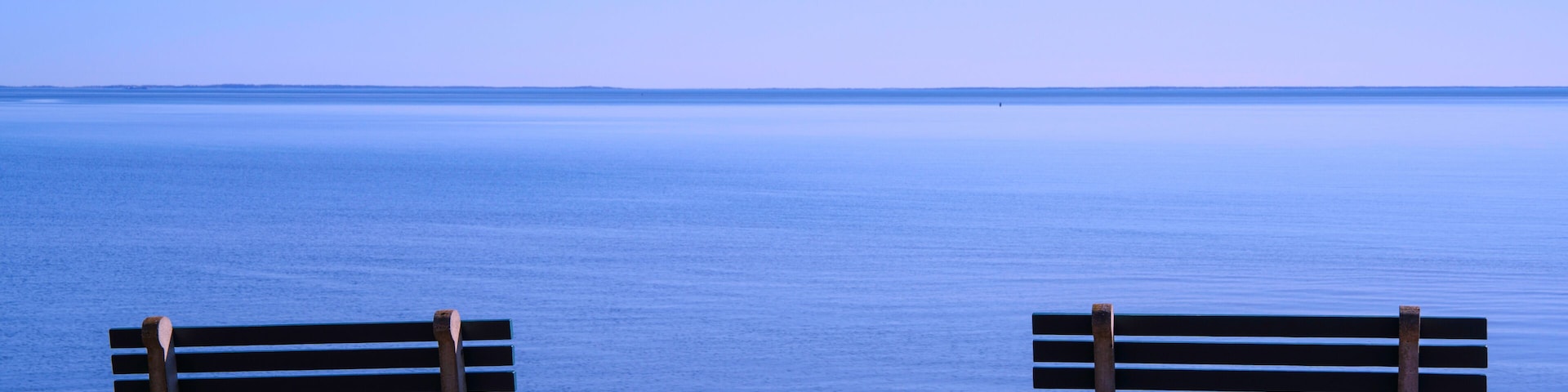 Seascape with two empty benches, a peaceful beach scenery with blue water and sky