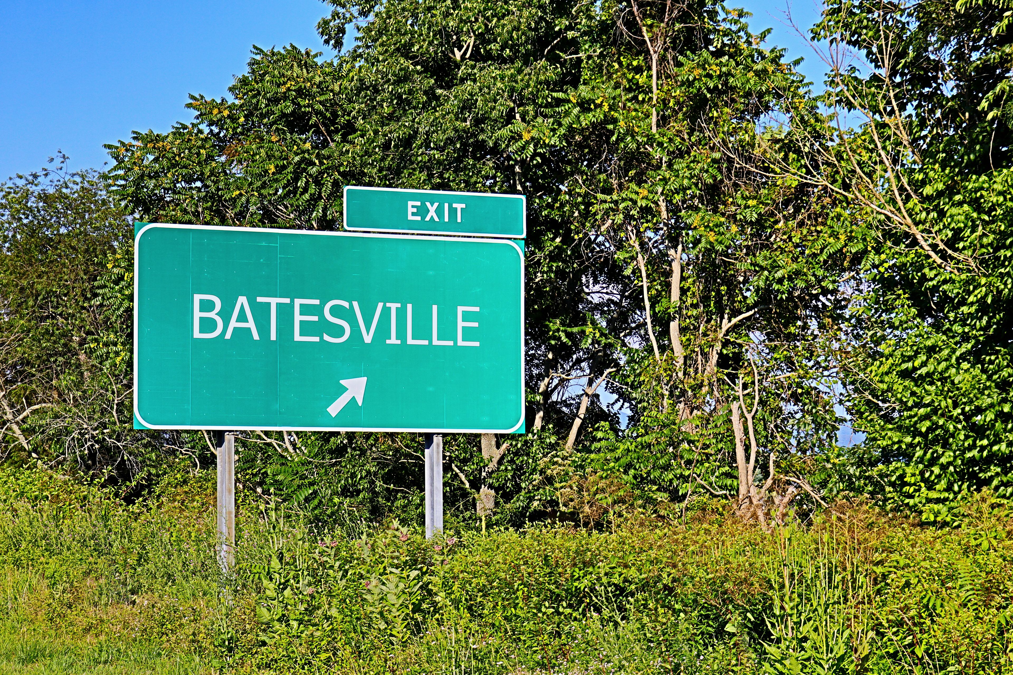 A green highway sign for Batesville with an arrow pointing right, surrounded by lush greenery and trees.