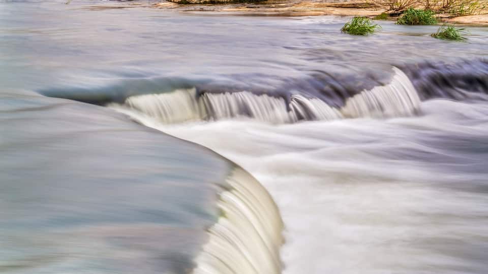 A red covered bridge over a flowing river with a waterfall.