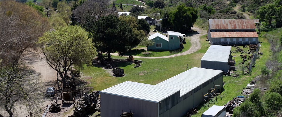 A rural landscape with rolling hills, a winding road, and several buildings including a house and barns.