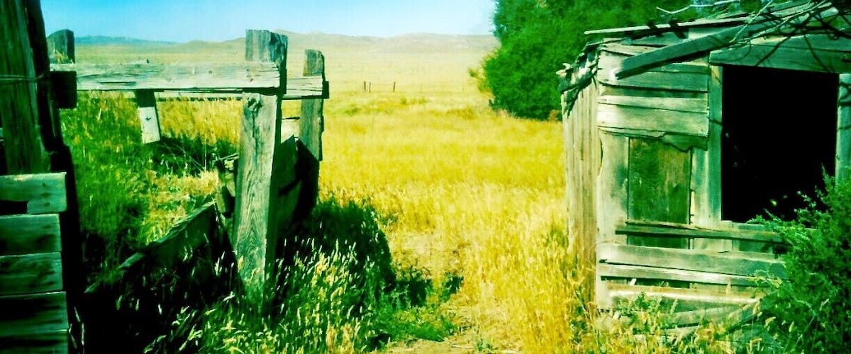 A rural landscape with a wooden fence, a small wooden structure, and a clear blue sky.