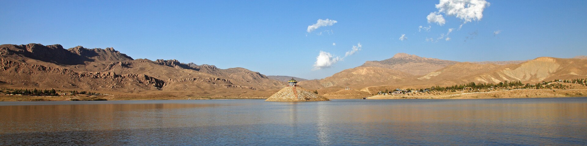 Un lago tranquilo con montañas al fondo y un cielo azul despejado.