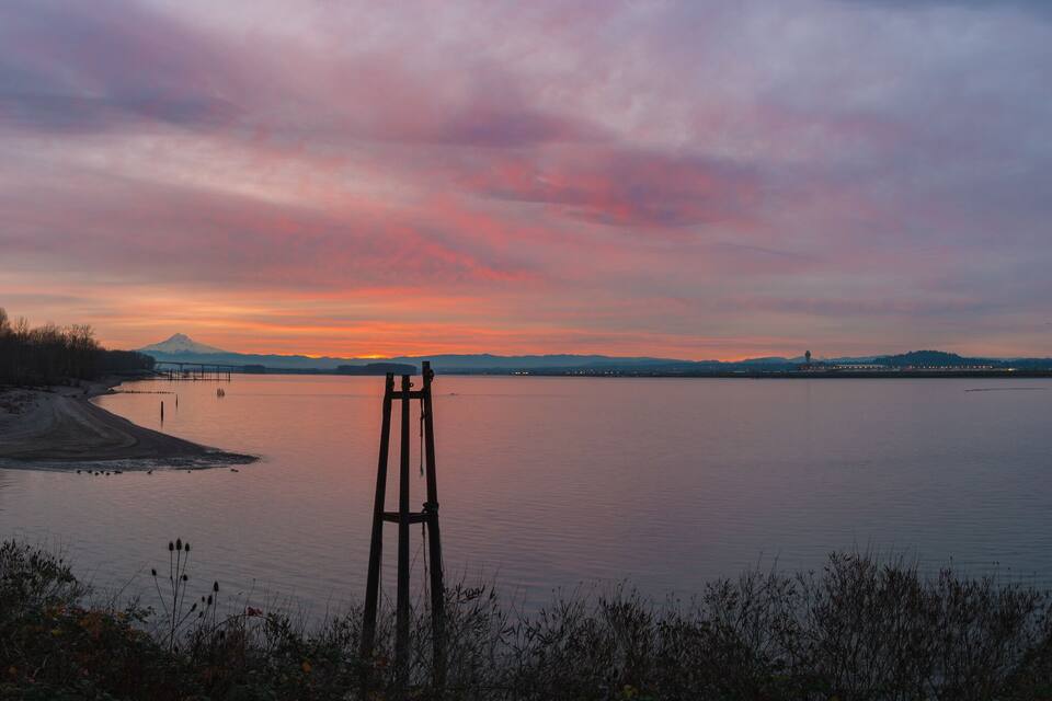 A sunset over a calm lake with a wooden structure in the foreground and mountains in the background.