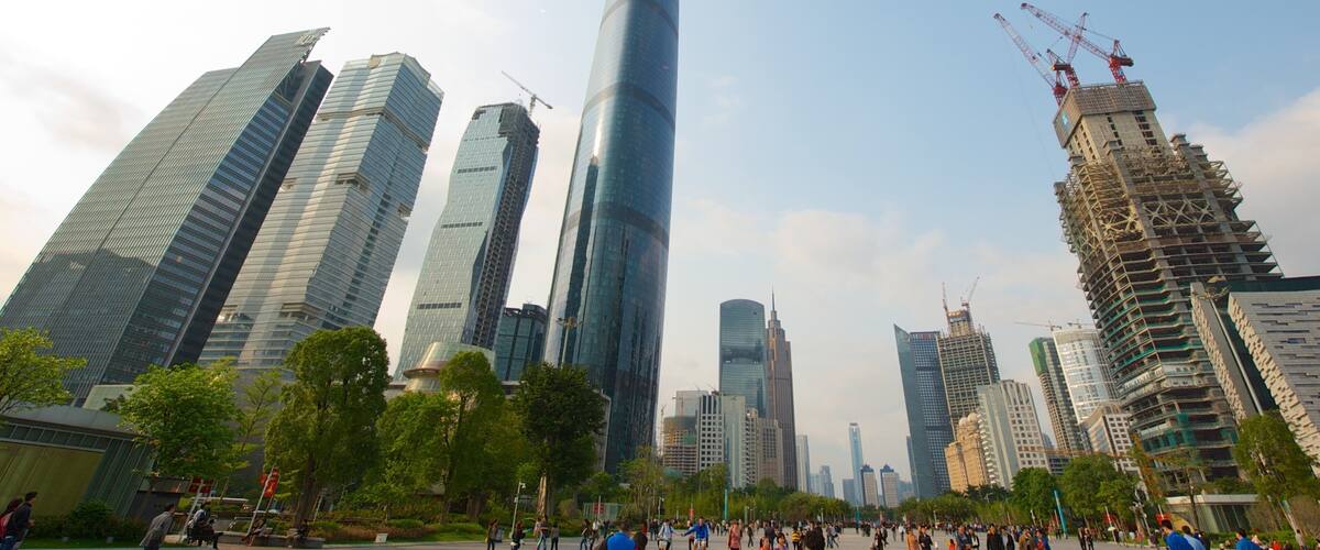 A cityscape with modern skyscrapers, a large curved building, and construction cranes.