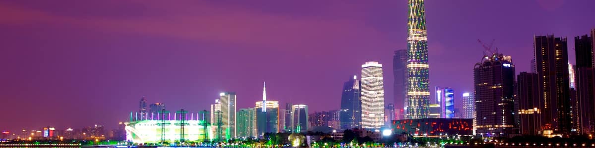 A city skyline at night with illuminated buildings and a river reflecting the lights.