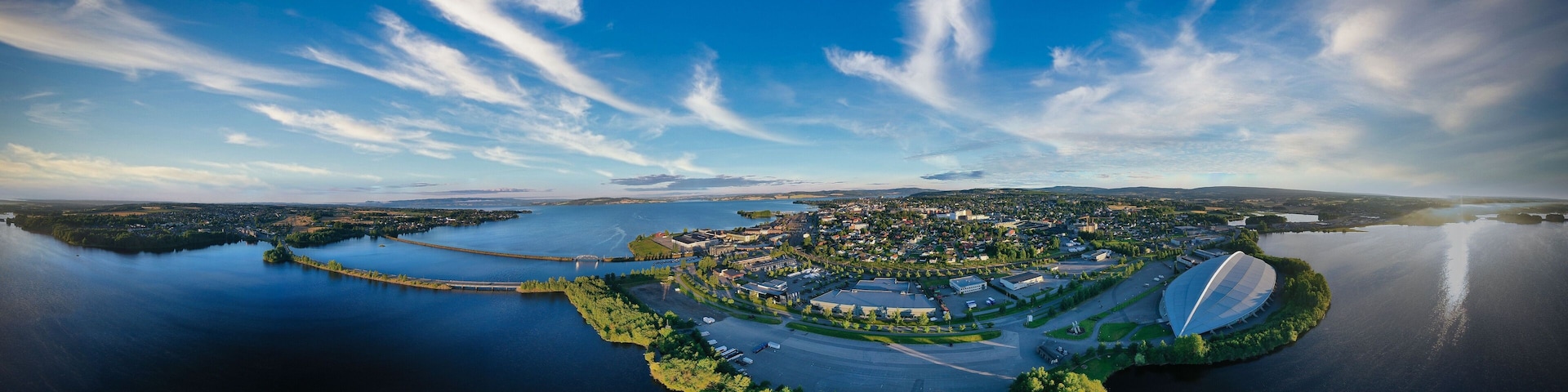 An aerial view of a city with a large stadium, a river, and surrounding greenery.